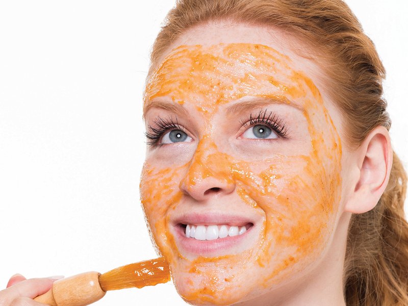 Fille avec un pinceau met un masque de carottes sur son visage Fille avec un pinceau met un masque de carottes sur son visage