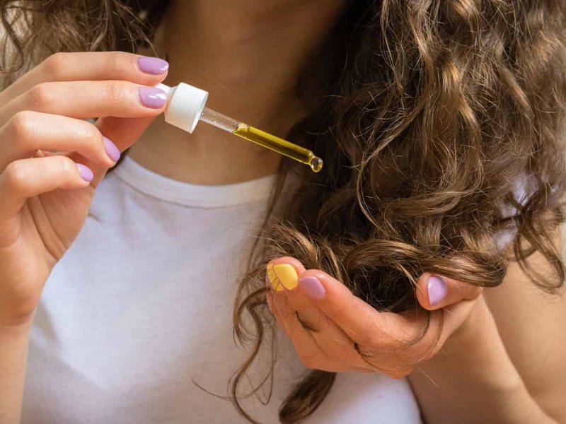 Fille utilise de l'huile de jojoba au bout de ses cheveux